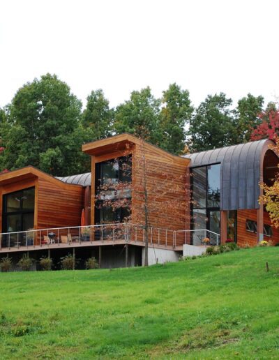 Modern wooden house with curved features surrounded by autumn foliage.