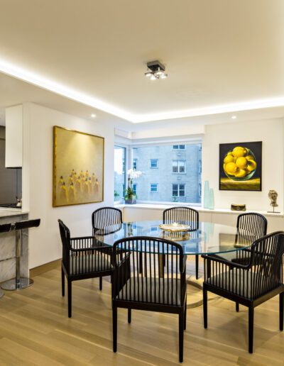 Modern kitchen and dining area with marble island, glass table, and black chairs, illuminated by ceiling lights.