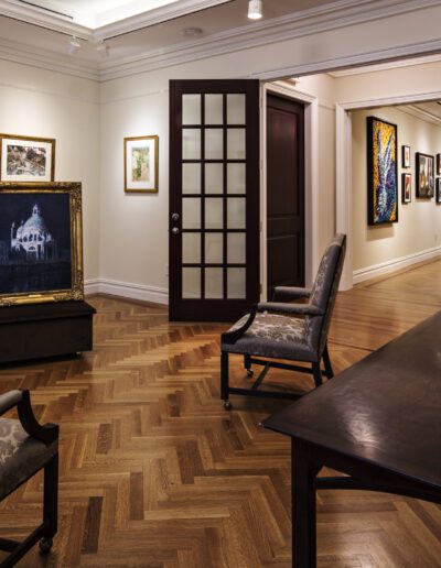 Elegant interior of an art gallery room with paintings on the walls and an orchid arrangement on a table.