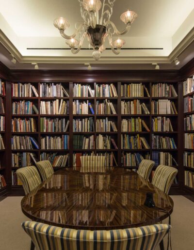 An elegant home library with floor-to-ceiling bookshelves and a polished wooden table surrounded by striped chairs.