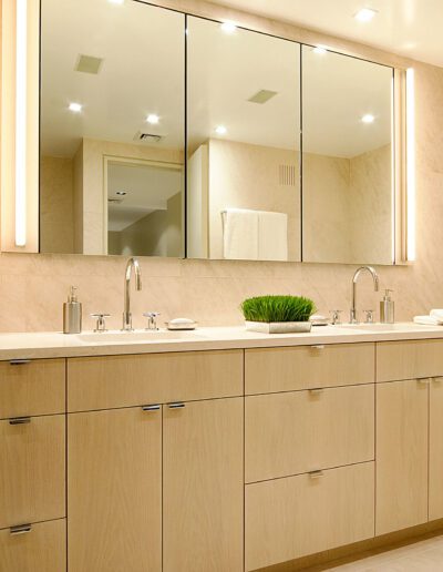 Modern bathroom interior with a large mirror, double sink vanity, and beige marble walls.